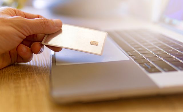 a person holding their credit card to their laptop